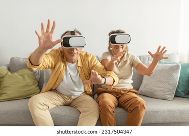 Virtual adventures concept. Modern senior spouses engaging in vr fun playing game, wearing headsets, sitting on couch at home. Innovative entertainment - Powered by Shutterstock