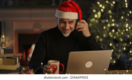 Virtual Christmas online - Happy smiling middle aged man in Santa hat at home video chatting with family on laptop computer, talking, waving hand. Cosy room with fireplace in winter. - Powered by Shutterstock