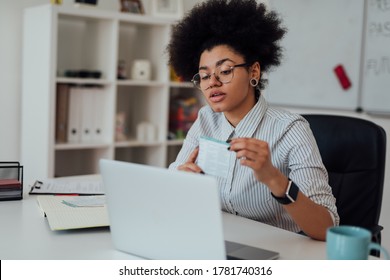 Virtual Classroom. Young Afro American Female Teacher Explaining Something While Teaching Through Webcam At Home. Sitting At Her Workplace And Looking At Camera. E-learning. Distance Education