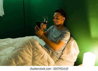 Virtual Date At Night. Cheerful Man Drinking Wine And Laughing While Making A Video Call With His Partner Before Going To Sleep 