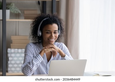 Virtual English Lesson. Biracial Female Sit By Desk In Headphones Watch Video Class On Laptop Listen To Mentor Explaining New Material. Young Black Lady Student Meet Teacher Online To Get Consultation