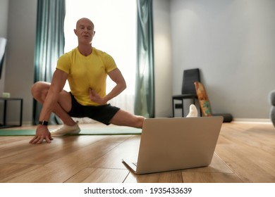 Virtual Fitness Class. Mature Personal Trainer In Sportswear Exercising And Looking At Laptop While Conducting Online Training At Home. Sport And Healthy Lifestyle Concept