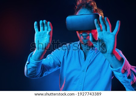 Virtual glasses gaming experience. Neon lighting. Young european man is in the dark studio.