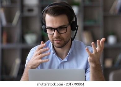 Virtual helpdesk. Young man in eyewear and wireless headset call center agent give technical support to customer. Male telemarketer speak by video call look on pc screen offer goods service to client