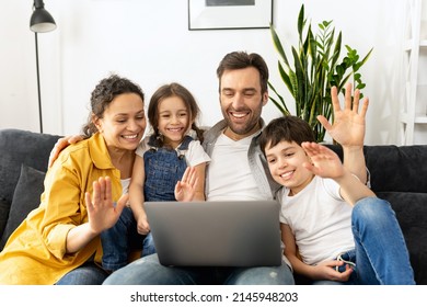 Virtual Meeting. Family Of Four Waving To Screen While Using Laptop For Video Connection With Grandparents Or Family. Multiracial Mom, Dad And Two Kids Waving In Webcam Of The Laptop, Video Call