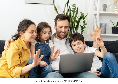 Virtual Meeting. Family Of Four Waving To Screen While Using Laptop For Video Connection With Grandparents Or Family. Multiracial Mom, Dad And Two Kids Waving In Webcam Of The Laptop, Video Call