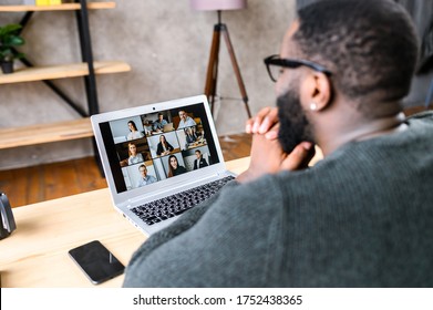 Virtual meeting with many people together. African-American young guy talking online with employees via video connection. Multiracial team. Back view