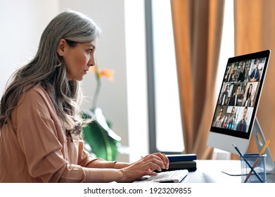 Virtual Meeting, Online Business Meeting. Serious Asian Mature Gray-haired Woman Communicate With Business Partners By Video Call Uses App And Computer, Sitting At Her Work Desk