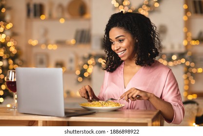 Virtual Meeting. Smiling African American Woman Sitting At Dining Table, Having Dinner, Eating Pasta, Having Video Call With Boyfriend, Friends Or Family On Laptop. Stay Home, Quarantine Celebration