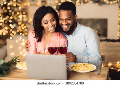 Virtual Party Concept. Smiling African American Couple Sitting At The Table And Having Online Video Call With Friends Or Family Using Laptop, Drinking Wine And Toasting, Celebrating Together At Home