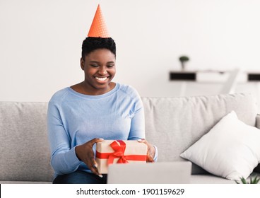 Virtual Party. Positive Cheerful African American Woman Wearing Hat, Showing Wrapped Gift Box With Present To Computer Webcam While Having Online Video Conference, Congratulating Friend With Holiday