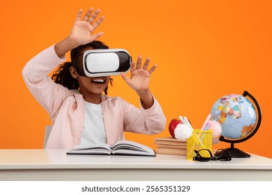 Virtual Reality Concept. Portrait of excited African American girl in VR headset touching air at yellow studio, copy space. Positive teen exploring artificial computer world sitting at desk