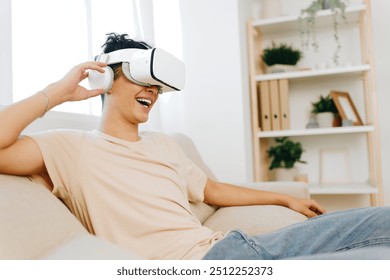 Virtual reality experience, young man enjoying VR headset, sitting on a cozy couch in a bright room with plants and shelves Fun and immersive technology exploration - Powered by Shutterstock