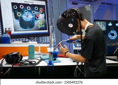 Virtual Reality Technology In Steel Industry 4.0. Man Wearing VR Glasses To See Simulate Welding Steel Pipe For Training, Measurement And Analytic To Monitor Screen In Smart Factory.