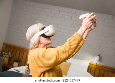  Virtual Reality. VR, Future, Gadgets. Senior Woman Playing Game In Virtual Reality Glasses And Holds Joysticks At Home