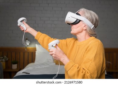  Virtual Reality. VR, Future, Gadgets. Senior Woman Playing Game In Virtual Reality Glasses And Holds Joysticks At Home