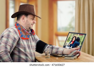 Virtual Rural Doctor Takes Cowboy Blood Pressure On-line. Physician Gives Thumb Up In Monitor. Man In Brown Hat Sits At Wooden Desk And Checks His Blood Pressure Before Taking Prescription Pills