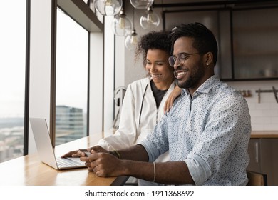 Virtual shoppers. Loving black spouses make purchases online pay for ordered consumer goods in laptop application using credit card. Smiling african married couple check electronic wallet bank account