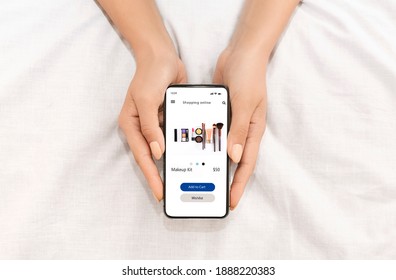 Virtual Shopping Concept. Above Top Overhead View Of Woman Holding And Showing Her Smartphone With Online Store On The Screen, Ordering Makeup Kit. Female Customer Ordering Via Internet