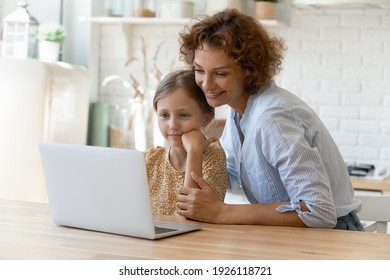 Virtual shopping. Smiling single mom help child junior girl choose school supplies at online web store. Bonding adult mother and daughter kid sit by kitchen table watch funny video in app on laptop pc
