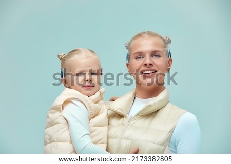 Virtual technology. Happy delighted nice girl smiling and looking at camera while mother holding in her arms wearing digital virtual glasses on biege background