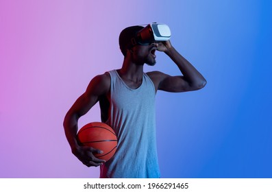 Virtual Workout Concept. Excited Millennial Black Athlete In VR Headset Holding Basketball In Neon Light. Emotional Young Sportsman Using Modern Technologies For His Training