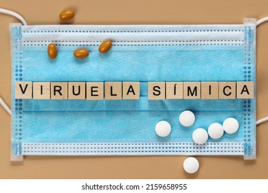 Viruela símica is the name of the monkeypox virus in Spanish. The word is laid out with wooden cubes on a surgical face mask. There are various pills lying around. - Shutterstock ID 2159658955