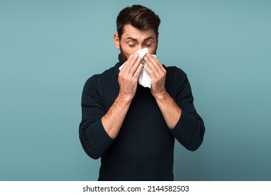 Virus outbreak, flu epidemic. Man sneezing in napkin, cleaning running nose and coughing, suffering influenza symptoms, fever. Indoor studio shot isolated on blue background  - Powered by Shutterstock