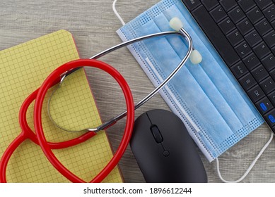 Virus Pandemic And Medical Concept With A Colorful Red Stethoscope Coiled Over A Surgical Face Mask Alongside A Notebook On A Wooden Desk With Computer Keyboard Viewed Top Down