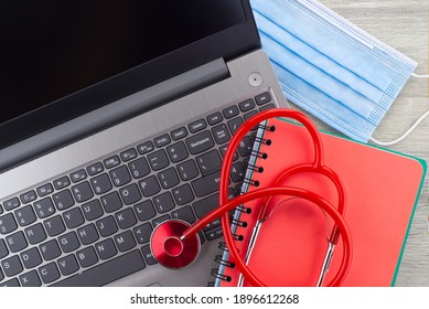 Virus Pandemic And Medical Concept With A Colorful Red Stethoscope Coiled Over A Surgical Face Mask Alongside A Notebook On A Wooden Desk With Computer Keyboard Viewed Top Down