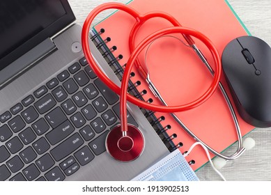 Virus Pandemic And Medical Concept With A Colorful Red Stethoscope Coiled Over A Surgical Face Mask Alongside A Notebook On A Wooden Desk With Computer Keyboard Viewed Top Down