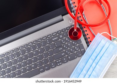 Virus Pandemic And Medical Concept With A Colorful Red Stethoscope Coiled Over A Surgical Face Mask Alongside A Notebook On A Wooden Desk With Computer Keyboard Viewed Top Down