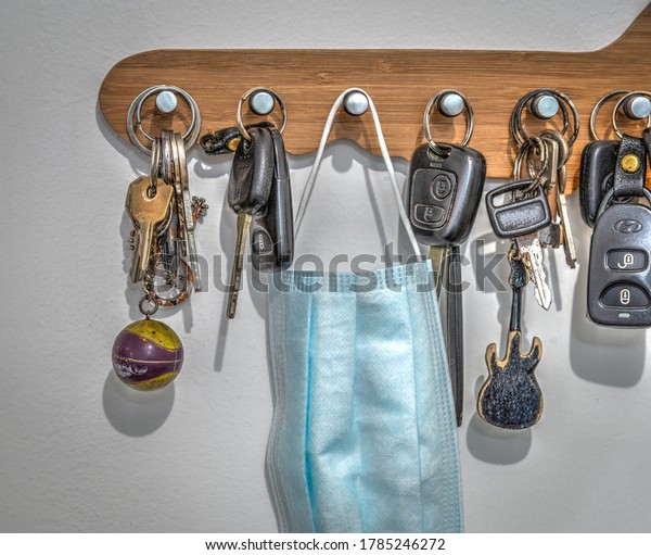 Virus protection mask
among car and house keys hanging on a white wall. Ready to be taken
outside the house for protection against the Coronavirus. Covid-19
pandemic 2020