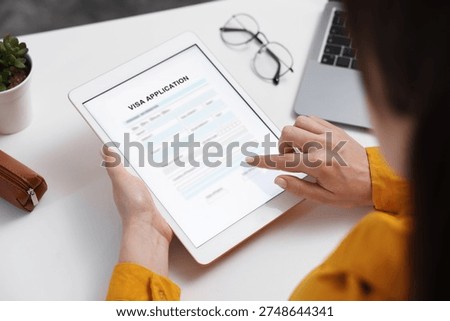 Visa application. Woman using tablet computer to fill in online form at table, closeup