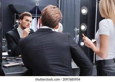 visage artist holding face powder near man looking in mirror in makeup room
