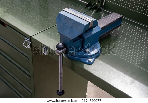 Vise grip stationary. Steel vise fixed on table.\
Tool for mechanical work. Mechanics desktop. Mechanical equipment\
for auto mechanic. Blue vise close-up. Concept sale of equipment\
for mechanic