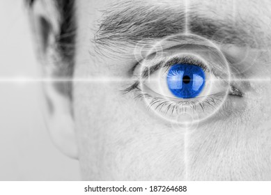 Vision concept with a greyscale image of a mans eye with a crosshair focused on his iris which has been selectively colored blue.