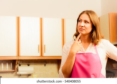 Vision and idea concept. Thinking wondering woman in kitchen. Contemplating housewife wearing pink apron at home.