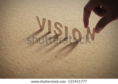 VISION wood word on compressed board with human's finger at N letter