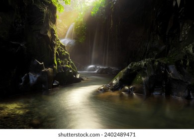 Visit the charm of Indonesia with the Lorong Watu waterfall, North Bengkulu. A narrow alley lined with stone walls, the morning light shines on the waterfall - Powered by Shutterstock