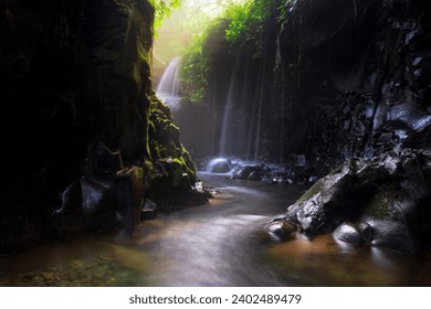 Visit the charm of Indonesia with the Lorong Watu waterfall, North Bengkulu. A narrow alley lined with stone walls, the morning light shines on the waterfall - Powered by Shutterstock