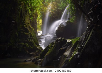 Visit the charm of Indonesia with the Lorong Watu waterfall, North Bengkulu. A narrow alley lined with stone walls, the morning light shines on the waterfall - Powered by Shutterstock