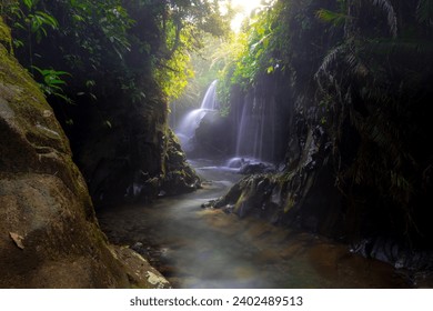 Visit the charm of Indonesia with the Lorong Watu waterfall, North Bengkulu. A narrow alley lined with stone walls, the morning light shines on the waterfall - Powered by Shutterstock