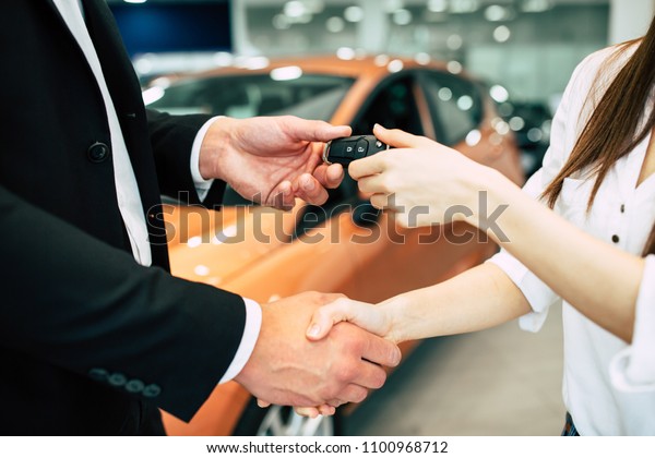The visit to the dealership ended with the\
purchase of a car. The seller hands over the keys to the buyer on\
the back of a car\
dealership