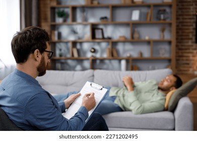 A visit to the psychologist of an African American man. A handsome man is lying on the couch and talking to a psychotherapist. Depression, apathy, stress, burnout at work. Help of a psychologist. - Shutterstock ID 2271202495