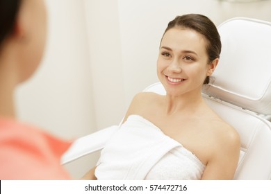 Visiting Beautician. Gorgeous Young Woman Smiling While Talking To Her Cosmetologist At The Beauty Clinic Spa Treatment Therapist Skin Face Body Care Revitalizing Profession Job Occupation Industry