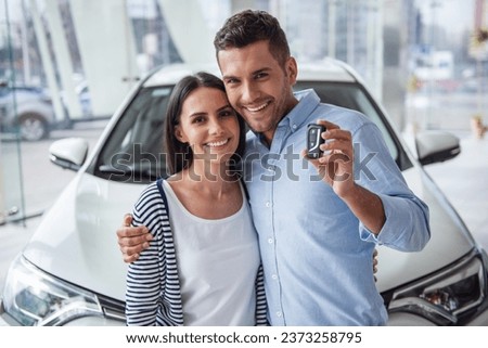 Visiting car dealership. Beautiful couple is holding a key of their new car, looking at camera and smiling