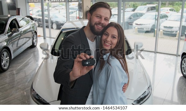 Visiting car dealership.\
Beautiful couple is holding a key of their new car, looking at\
camera and smiling.