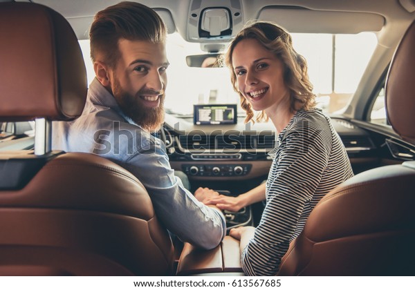 Visiting car dealership.\
Beautiful couple is looking at camera and smiling while sitting in\
their new car