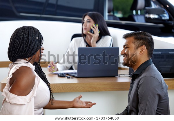 Visiting a car
dealership choosing and buying a new car. A young emotional
African-American married couple communicate against the background
of a car sales agent. Selective
focus.